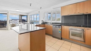 A modern kitchen with wooden cabinets, a black countertop, a stainless steel oven, and a dishwasher. - Walk to Beach • Luxury Waterfront Sub-Penthouse (Sunshine Coast)