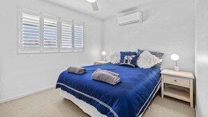 A bedroom with a bed, two bedside tables, a ceiling fan, and a window with blinds. - Walk to Beach • Luxury Waterfront Sub-Penthouse (Sunshine Coast)