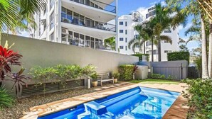 A swimming pool with a wooden deck, surrounded by a garden with small plants and a bench. - Walk to Beach • Luxury Waterfront Sub-Penthouse (Sunshine Coast)