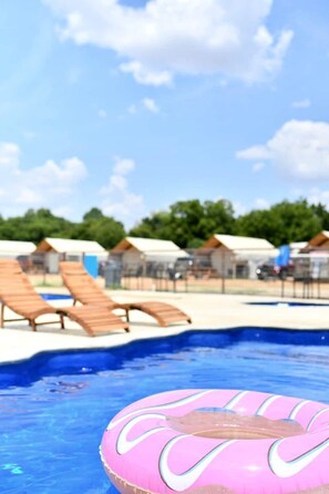 A swimming pool with lounge chairs and a pink inflatable ring. - Water Sports Galore at this Fully-Equipped Safari Tent in Cibolo, Texas (Marion)