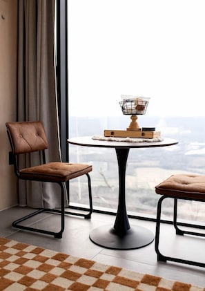 Una habitación moderna con vistas, que incluye una mesa redonda con un candelabro, dos sillones tapizados y una alfombra a cuadros.