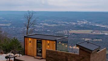 A modern cabin with a wooden exterior, a deck, and a glass enclosure.