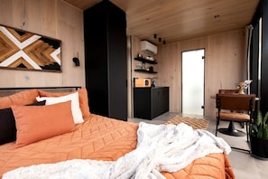 A modern bedroom with a large bed, a black wardrobe, a kitchenette, and a view of the outside. - Stunning Mirrored Glass Cabin with Hot Tub & Sauna near Lookout Mountain, Dade County, GA (Dade County)