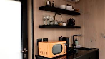 A compact kitchen with a microwave, shelves with dishes and glasses, and a coffee maker.