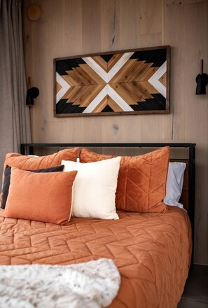 Un lit avec une tête de lit en bois, une œuvre d’art murale aux motifs géométriques et une lampe noire.