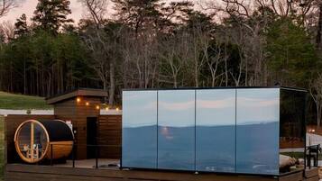 A cabin with a large glass wall, a wooden deck, and a circular skylight.