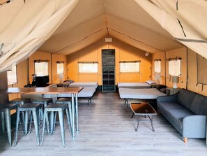 Eine Zelthotelunterkunft mit einem zentralen Tisch, Barhocker, einer Couch und einem Bett.