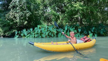 A person in a yellow inflatable raft on a calm river surrounded by dense green foliage.