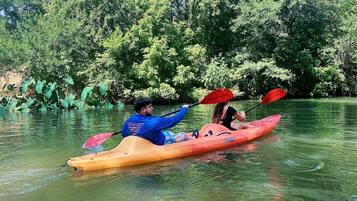 Zwei Personen paddeln in einem ruhigen Fluss, umgeben von dichtem Grün.