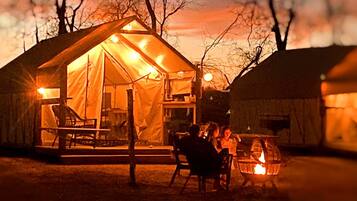 A tented accommodation with a fire pit, outdoor seating, and a view of the surrounding trees.
