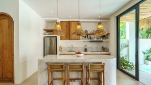 A modern kitchen with a central island, bar stools, hanging wicker pendant lights, and a view of a pool through large sliding doors. - Stunning 3BR Villa • Rooftop Pool • 3min to Beach Balangan (Badung)