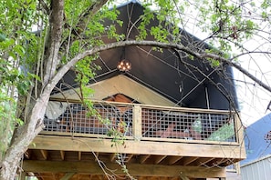 Un balcon en bois avec une balustrade en métal, un auvent noir et un arbre au premier plan.