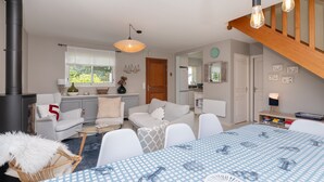 Una sala de estar acogedora con chimenea, una mesa de comedor con mantel azul y una escalera que lleva a otro nivel.