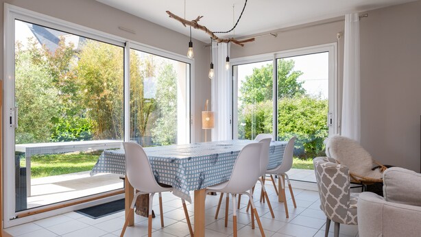 Comedor con mesa, sillas y vista a la vegetación a través de grandes ventanales.