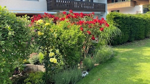 En tvåvåningsbyggnad med en balkong, omgiven av frodig grönska och blommande växter.
