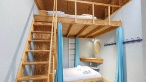 Ein Schlafraum mit Etagenbetten und einer Holzleiter, ein kleines Badezimmer mit Spiegel und Waschbecken.