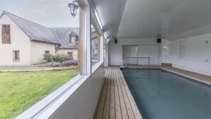 Ein Hallenbad mit Holzterrasse, Blick auf ein Haus und einer Tür.