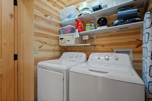 A laundry area with two white washing machines, a shelf with various items, and a wooden wall. - Fireworks view, half mile to Dollywood, Hot Tub, Firepit, Fully stocked Kitchen (Pigeon Forge)
