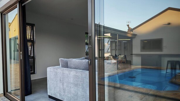 A modern living room with a grey sofa, a glass door leading to a pool area, and a view of the backyard.