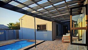 A covered outdoor area with a swimming pool, a patio with brick flooring, and a glass door leading to an interior space.