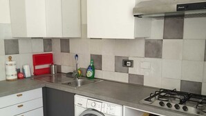 Una cucina compatta con mobili bianchi, lavatrice, piano cottura a gas e forno a microonde.
