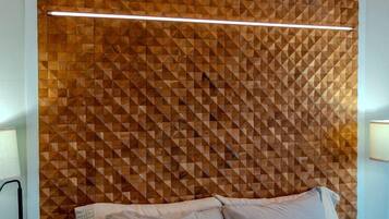 A bedroom with a geometric-patterned headboard, a bed with light-colored bedding, and a bedside table with a lamp.