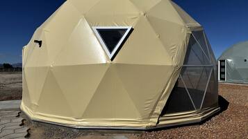 A geodesic dome structure with a triangular window, a door, and a small vent.