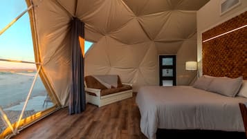A tent-style room with a bed, a chair, a small table, and a window.