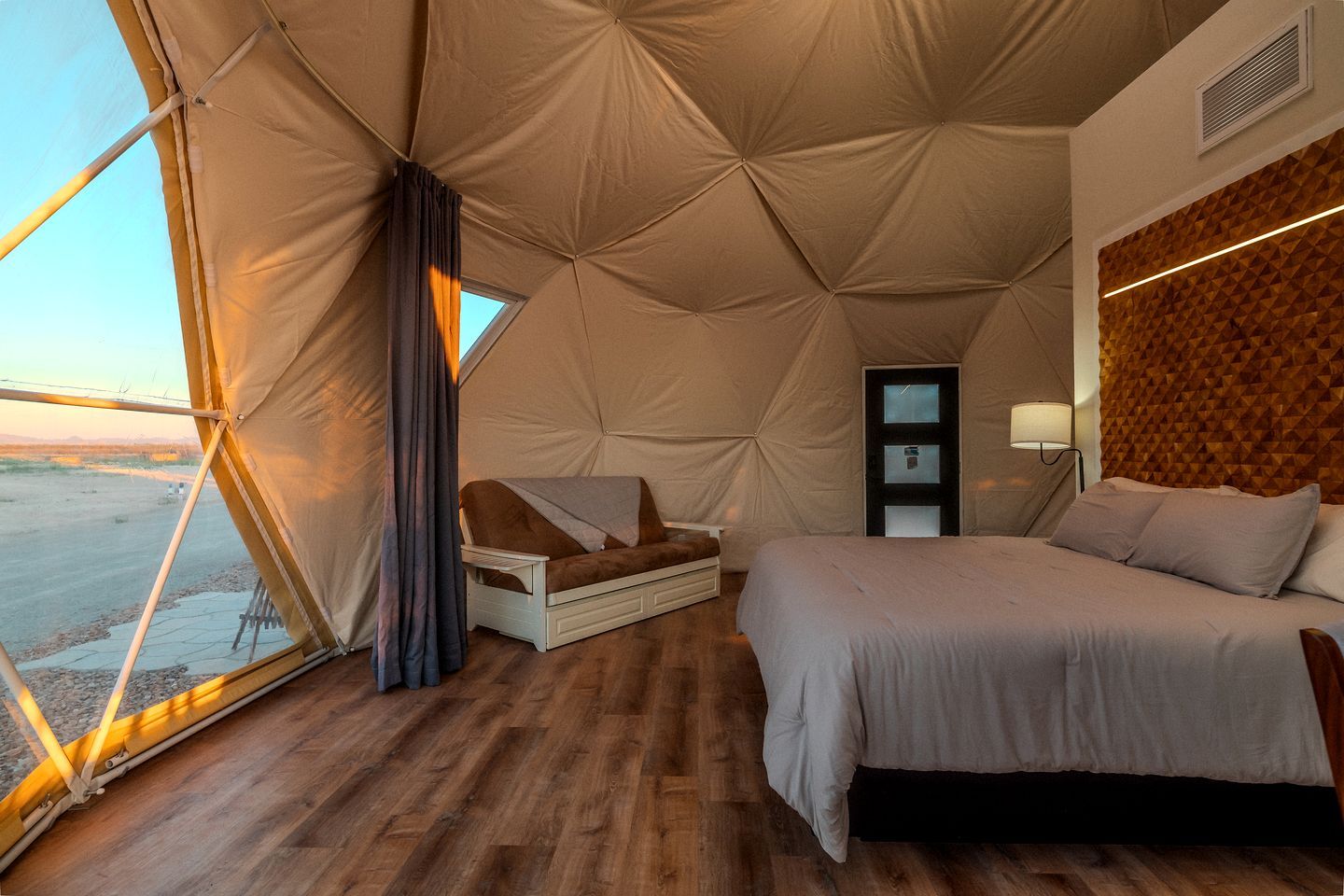 A tent-style room with a bed, a chair, a small table, and a window.