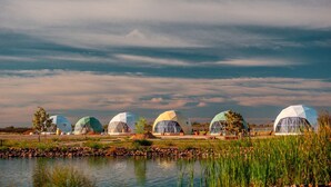 A row of geodesic dome structures by a body of water with a cloudy sky.