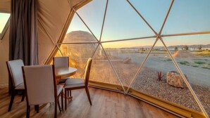 A tent with a dining area and a view of a desert landscape.
