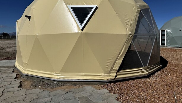 A geodesic dome structure with a triangular window, a door, and a small vent.