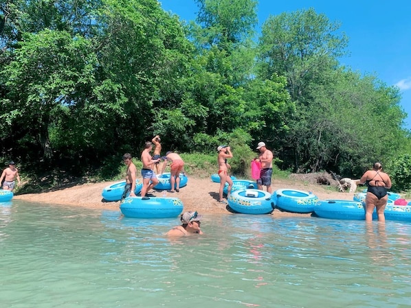 People in a natural setting with water and trees, some on inflatable rings.