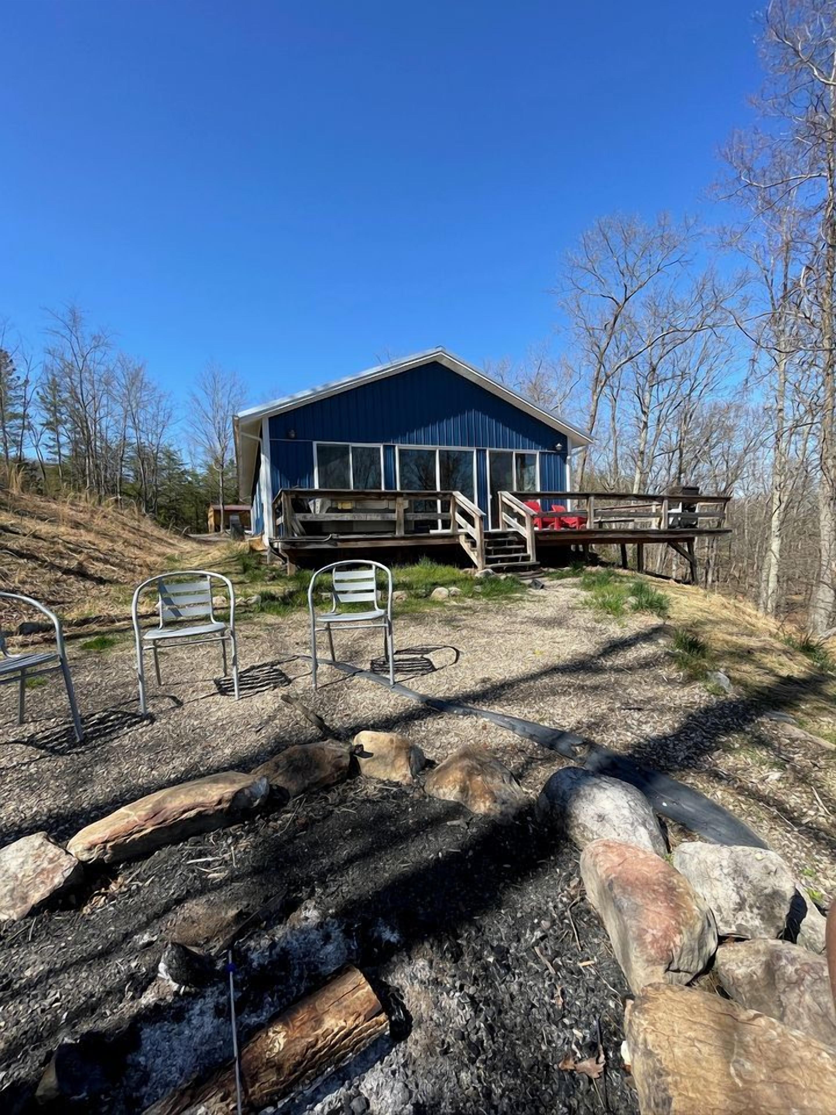 A blue building with a porch, metal chairs, and a fire pit area.