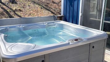 A hot tub on a wooden deck with a blue building in the background.