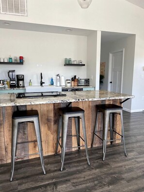 Una cocina con encimera de mármol, tres taburetes de bar, una cafetera y un tostador.