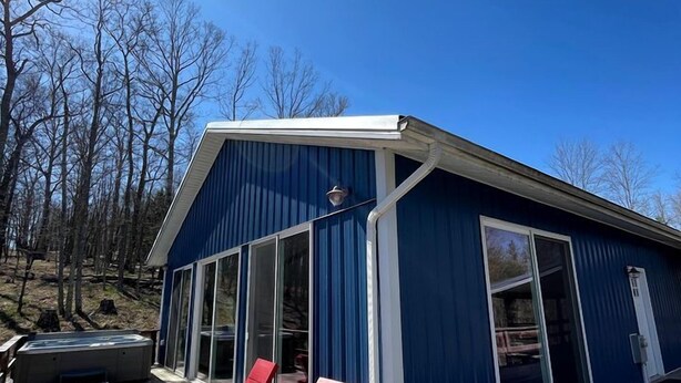 A blue building with a deck, two red chairs, and a hot tub.