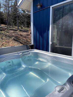 A hot tub with a clear view of the surrounding area, including a blue building and a forested landscape. - Relaxing Converted Barn Surrounded by Nature near Lost River, West Virginia (Mathias)