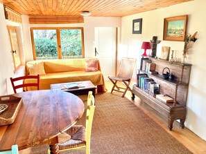 Une pièce chaleureuse avec un plafond en bois, un canapé, une table à manger, une bibliothèque et une fenêtre donnant sur un paysage verdoyant.