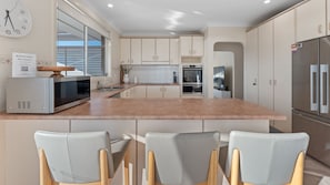 A modern kitchen with a central island, built-in appliances, and a seating area with chairs. - Betsy's Batch Family Holiday Home Soldiers Point (Soldiers Point)
