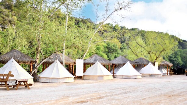 A row of white tents with thatched roofs, arranged on a sandy surface with trees in the background. - Glamping Adventure on the Guadalupe River: Cool Bell Tent near New Braunfels, Texas Perfect for All Ages (New Braunfels)