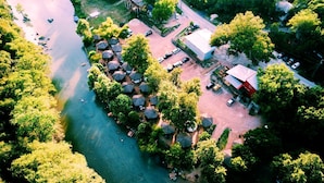 An aerial view of a riverside property with a cluster of thatched-roof huts, a main building, and a parking area. - Glamping Adventure on the Guadalupe River: Cool Bell Tent near New Braunfels, Texas Perfect for All Ages (New Braunfels)