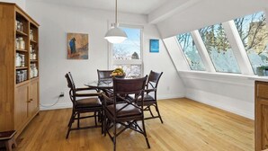 Een eetgedeelte met een ronde tafel, donkerhouten stoelen, een hanglamp en uitzicht door een dakraam.