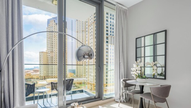 A modern room with a large window, a round table with chairs, a potted orchid, and a mirror on the wall. - LUX LIV Contemporary Skyline Studio (Dubai)