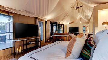 A tented room with a bed, a flat-screen TV, a desk, and a chair.