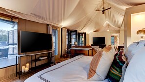 A tented room with a bed, a flat-screen TV, a desk, and a chair.