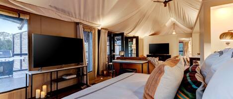 A tented room with a bed, a flat-screen TV, a desk, and a chair.