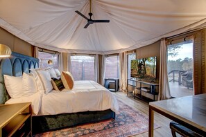 Ein Zelttraumzimmer mit Bett, Deckenventilator, Fernseher und Blick ins Freie.
