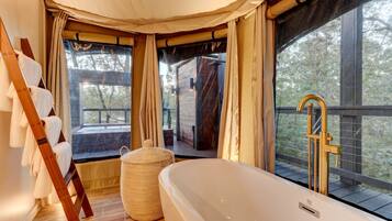 A bathroom with a bathtub, wooden ladder, and a large window with curtains.