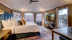 Ein Zelttraumzimmer mit Bett, Deckenventilator, Fernseher und Blick ins Freie.